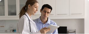 A female doctor showing information on a digital tablet to a man in a medical office.